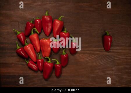 Mazzo di pepe rosso sulla scrivania in legno. Grande quantità di pepe rosso in un mucchio con uno fuori per una passeggiata Foto Stock