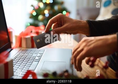 Concetto di persona che fa shopping di natale in linea a casa da un laptop con scheda. Vista frontale. Composizione orizzontale. Foto Stock