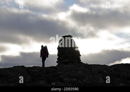 Silhouette di un Walker vicino al Cairn sulla cima di Artlecrag Pike, Branstree, Lake District, Cumbria, Regno Unito Foto Stock