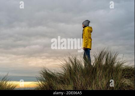 donna che indossa un cappotto giallo in piedi sulla cima di una duna, concetto di copertina del libro. Foto Stock