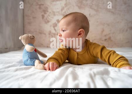 Vista dall'alto Ritratto di un neonato cute baby boy indossava un bodysuit infantile sul letto , affascinante bambino 5 mesi di età si trova a letto con una bambola, godere e felice Foto Stock