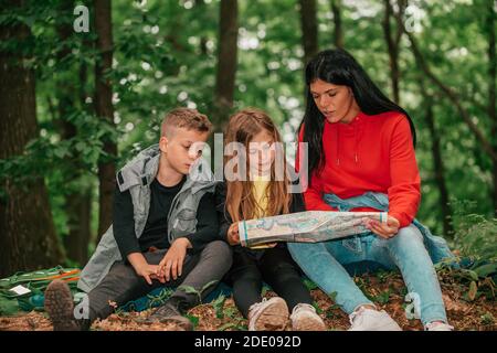 Bella madre con due bambini sono seduti nella foresta, utilizzando una mappa e la pianificazione di un'avventura escursionistica. Felice famiglia che si diverte Together.Selective fuoco Foto Stock
