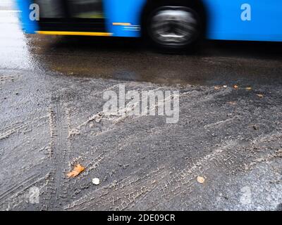 la prima neve sciolta sulla strada della città e autobus blu sfocato in movimento il giorno d'autunno Foto Stock