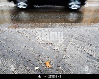 la prima neve sciolta sulla strada cittadina e auto nera sfocato in movimento il giorno d'autunno Foto Stock