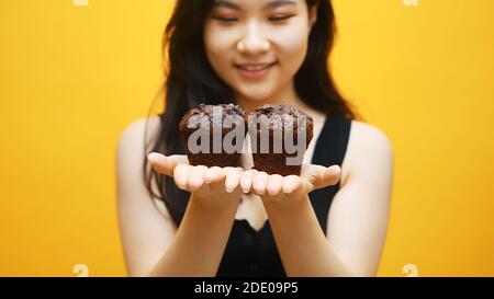 Muffin al cioccolato nelle mani di una bella giovane donna asiatica. Primo piano. Foto di alta qualità Foto Stock