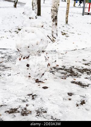 pupazzo di neve fatto dalla prima neve con foglie caduto dentro parco cittadino ghiacciato il freddo giorno d'autunno Foto Stock