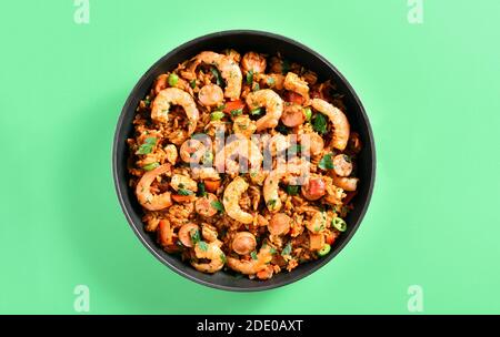 Vista ravvicinata della creola jambalaya con pollo, salsicce affumicate e verdure in padella su sfondo verde. Vista dall'alto, disposizione piatta, primo piano Foto Stock