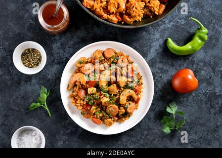 Creola jambalaya con riso, salsicce affumicate, carne di pollo e verdure su piatto su fondo di pietra blu. Vista dall'alto, disposizione piatta, primo piano Foto Stock