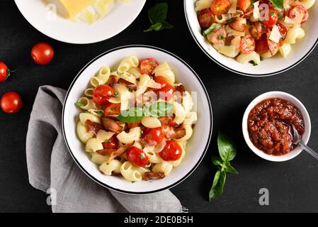 Pasta con pancetta, pomodoro, parmigiano e foglie di basilico sul piatto su fondo di pietra nera. Vista dall'alto, disposizione piatta Foto Stock