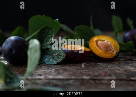 Prugne organiche fresche poste vicino alle foglie Foto Stock