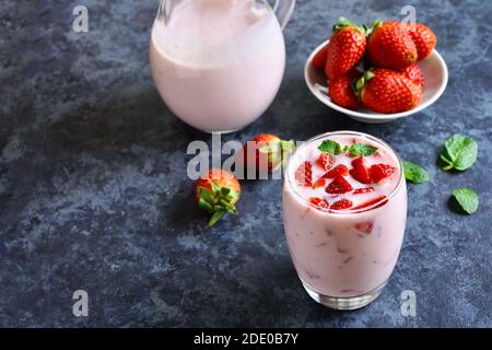 Yogurt alla fragola con frutti di bosco freschi in vetro su sfondo di pietra blu con spazio di testo libero. Concetto sano di cibo e bevande. Foto Stock