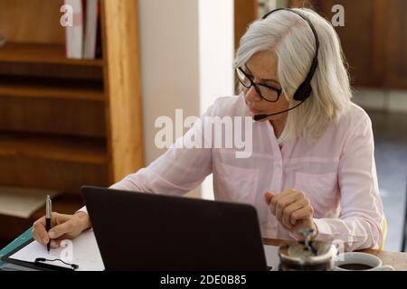 Donna caucasica anziana che usa un computer portatile e indossa le cuffie Foto Stock