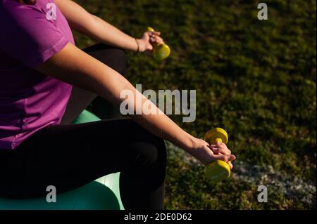 Donna seduta su fitball e facendo esercizi con manubri Foto Stock