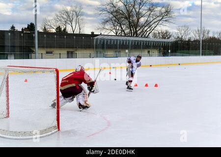 i giocatori di hockey dei giovani sparano su goalie durante l'hockey su ghiaccio all'aperto formazione Foto Stock