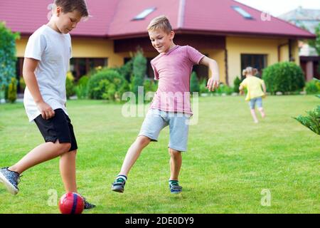 Due figli felici che giocano a calcio con il padre in giardino Vicino a Casa moderna Foto Stock