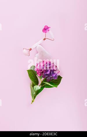 Composizione bilanciata con massaggiatore viso a rullo in giada rosa, raschietto di gouache su fiore di idrangea su sfondo rosa. Quarzo rosa. Anti età, sollevamento e. Foto Stock