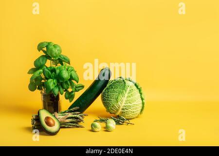 Composizione astratta con verdure fresche di cavolo, zucchine, asparagi, germogli di Bruxelles, avocado, basilico su fondo giallo. Vegetariano e. Foto Stock