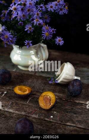 Delicati fiori blu in vaso bianco vicino alla prugna arancione Foto Stock