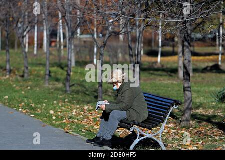 Bucarest, Romania. 27 Nov 2020. Una donna che indossa una maschera si siede sulla panchina di un parco nel centro di Bucarest, Romania, 27 novembre 2020. Le autorità rumene hanno imposto un coprifuoco di un mese in tutto il paese a partire dal 9 novembre. I residenti non sono autorizzati a lasciare le loro case dalle 11 alle 5 senza circostanze particolari. Credit: Cristian Cristel/Xinhua/Alamy Live News Foto Stock