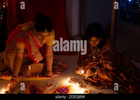 Due belle donne indiane bengalesi in abito tradizionale indiano che illumina Diwali diya / lampade seduta sul pavimento al coperto nel buio sulla sera di Diwali. Foto Stock