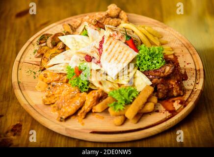 Gustosi spuntini deliziosi. Snack per la birra. Il cibo del ristorante. Tavola di legno con un sacco di patatine fritte bastoncini di pesce burrito e bistecca di carne con insalata mista. Ad alto contenuto calorico snack per il gruppo amici. Pub menu snack. Foto Stock