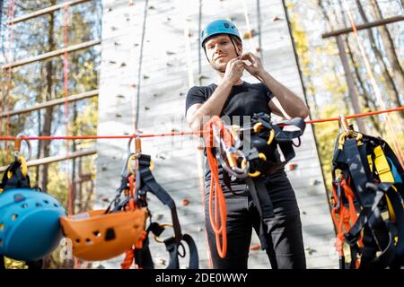 Bell'uomo che indossa attrezzature di sicurezza per l'arrampicata al parco divertimenti, preparandosi per l'arrampicata sulla parete Foto Stock