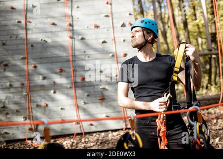 Bell'uomo che indossa attrezzature di sicurezza per l'arrampicata al parco divertimenti, preparandosi per l'arrampicata sulla parete Foto Stock