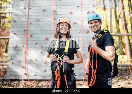 Ritratto di una giovane coppia ben attrezzata con equipaggiamento di sicurezza stare insieme di fronte alla parete di arrampicata al divertimento parcheggio Foto Stock