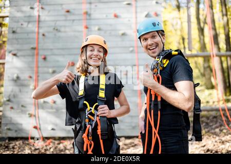 Ritratto di una giovane coppia ben attrezzata con equipaggiamento di sicurezza stare insieme di fronte alla parete di arrampicata al divertimento parcheggio Foto Stock