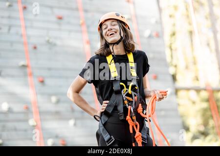 Ritratto di una giovane donna ben attrezzata in piedi davanti della parete di arrampicata al parco divertimenti Foto Stock