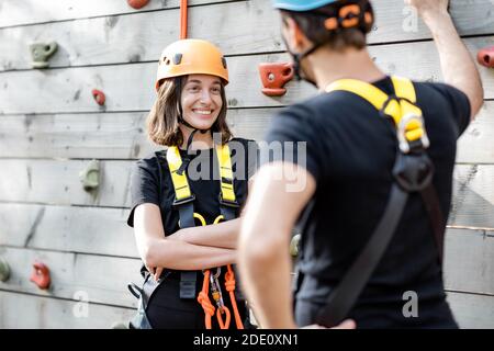 Sport Coppia ben attrezzata che parla e si diverte vicino alla parete di arrampicata, pronta per l'arrampicata al parco divertimenti Foto Stock