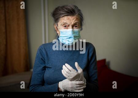 Ritratto la donna anziana ha preso misure di sicurezza, indossando guanti e maschera medica, prima della visita da parte degli operatori sociali durante la quarantena del coronavirus Foto Stock