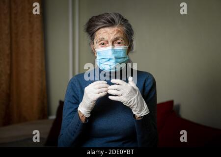 Ritratto la donna anziana ha preso misure di sicurezza, indossando guanti e maschera medica, prima della visita da parte degli operatori sociali durante la quarantena del coronavirus Foto Stock