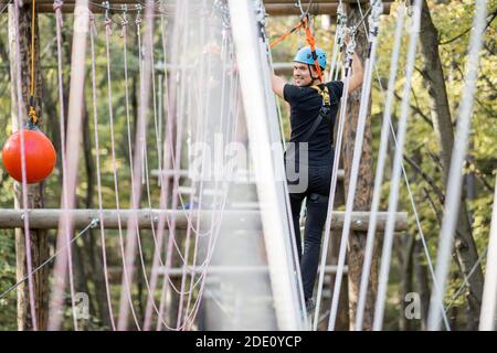 Uomo ben attrezzato che ha una ricreazione attiva, arrampicata in un parco di corda con ostacoli nella foresta Foto Stock