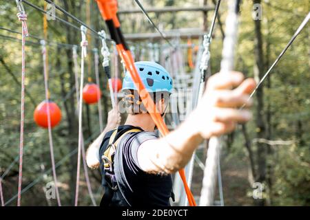 Uomo ben attrezzato che ha una ricreazione attiva, arrampicata in un parco di corda con ostacoli nella foresta Foto Stock