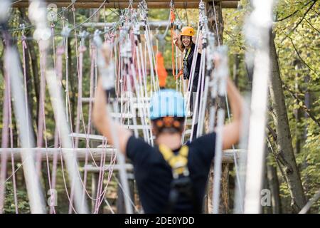 Uomo ben attrezzato che ha una ricreazione attiva, arrampicata in un parco di corda con ostacoli nella foresta Foto Stock