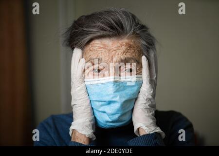 Ritratto di una donna caucasica anziana con rughe, indossando una maschera medica e guanti, l'emozione della fragilità e imprevedibilità dovuta al coronav Foto Stock