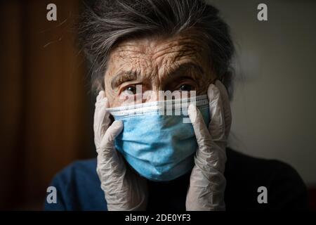 Ritratto di una donna caucasica anziana con rughe, indossando una maschera medica e guanti, l'emozione della fragilità e imprevedibilità dovuta al coronav Foto Stock