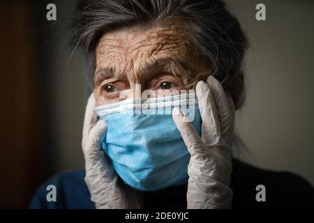 Ritratto di una donna caucasica anziana con rughe, indossando una maschera medica e guanti, l'emozione della fragilità e imprevedibilità dovuta al coronav Foto Stock