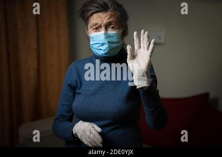 Guanto medico bianco in primo piano, mostrato da una nonna anziana che indossa una maschera medica, che chiede sicurezza e sanificazione durante un'epidemia. Senio Foto Stock