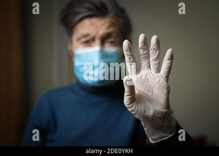 Importanza indossare guanti e maschere per proteggere il coronavirus, in particolare anziani e anziani. Focus su guanti in lattice su sfondo vecchia donna a medica Foto Stock