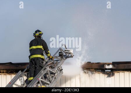 Vigili del fuoco che combattono un incendio da costruzione in cima a una scala estesa. Un tubo flessibile collegato alla scala riversa l'acqua nel tetto. Molto poco fumo. Foto Stock