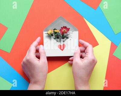 International grazie giorno. Biglietto d'auguri con le mani che tengono busta con cuore e fiori. Concept creativo piatto su sfondo di carta a strati. Foto Stock