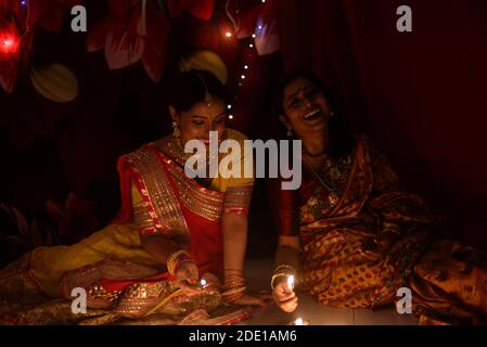 Due belle donne indiane bengalesi in abito tradizionale indiano che illumina le lampade Diwali seduta sul pavimento in serata Diwali. Stile di vita indiano Foto Stock