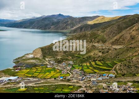 Orzo campo e villaggio sulla riva del lago Yamdrok (Yamdrok Yumtso), Tibet, Cina Foto Stock