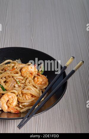 Tagliatelle di Udon con gamberi e verdure. Sfondo di legno. Vista dall'alto. Immagine verticale con spazio per la copia Foto Stock