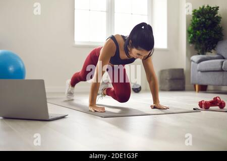 Giovane donna sportiva che guarda la video lezione e facendo affondare con guida al ginocchio a casa Foto Stock