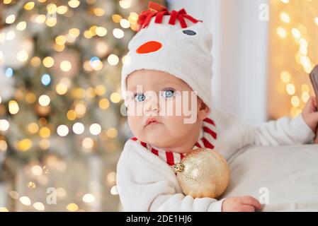 Bambino piccolo sotto l'albero di Natale. Bambino in cappello di pupazzo di neve con i regali sotto l'albero di Natale con molte scatole di regalo presenta. Buone feste, anno nuovo. Co Foto Stock