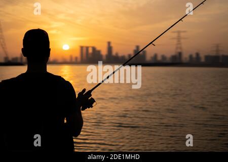 Il pescatore si stillava verso il tramonto e guarda lo skyline Di Abu Dhabi Foto Stock