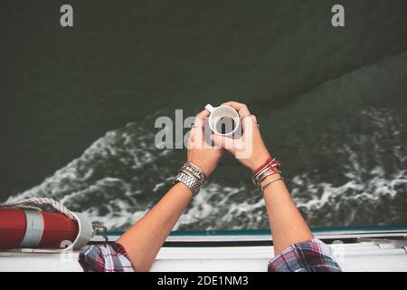 Una giovane donna prende il suo primo caffè del mattino sul ponte di una barca a Halong Bay, in Vietnam Foto Stock